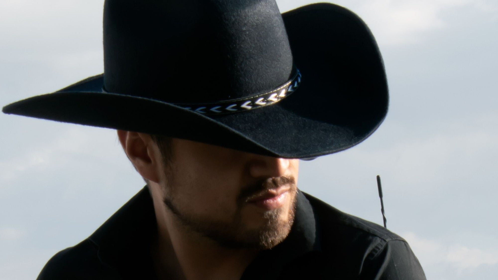 Person wearing a black cowboy hat against a cloudy sky