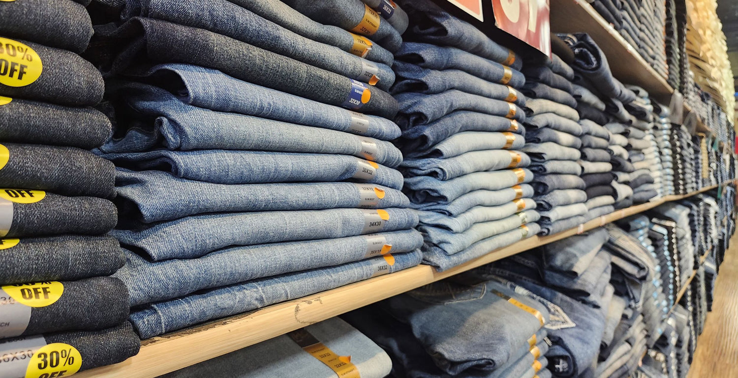 Stacks of folded jeans on a store shelf with promotional labels.